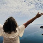 Woman with arms outstretched overlooking the ocean.