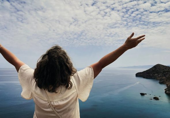 Woman with arms outstretched overlooking the ocean.
